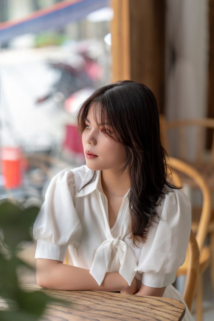 Young woman in a white blouse gazing outside in a cozy café setting.